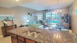 A kitchen with granite countertops, a sink, and a dining area with a table and chairs. - Saltwater Retreat, 2nd Floor, Spectacular Pool Area, Hot Tub, Free Beach Service (Miramar Beach)