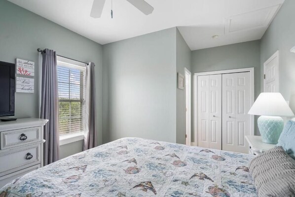 A bedroom with a bed, a dresser, a television, a window with curtains, and a door.