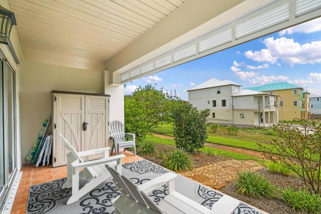 A covered porch with a bench and chairs, a door, and a view of neighboring houses.