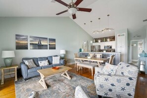 A living room with a sofa, coffee table, and a dining area with a table and chairs. There is a ceiling fan, a kitchen area, and artwork on the wall. - Free Amenities, Close To The Beach! Spyglass 105! (Destin)
