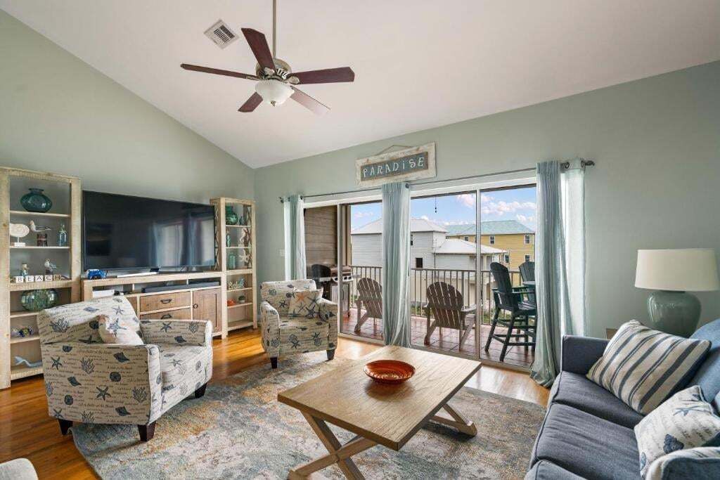 Ein Wohnzimmer mit Fernseher, zwei Sesseln, einer Couch, einem Couchtisch und einem Balkon mit Stühlen.