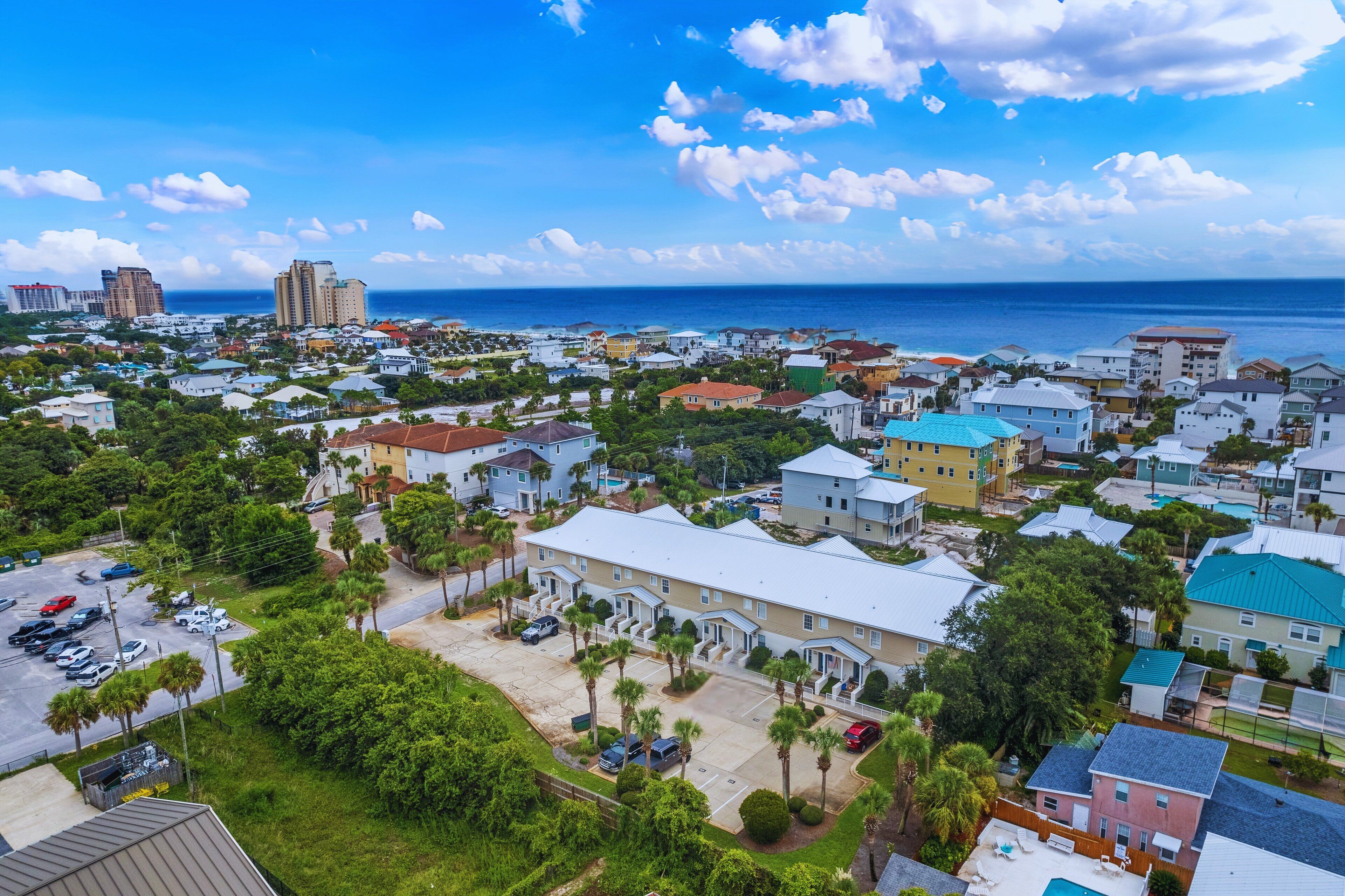 A coastal town with a mix of residential and commercial buildings, a parking lot, and a view of the ocean.