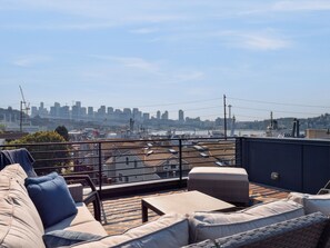 A rooftop terrace with outdoor seating, a view of a city skyline, and a clear sky.