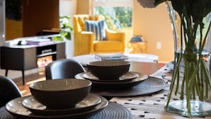 A dining table with bowls and a vase of flowers, a yellow armchair, and a television in the background.