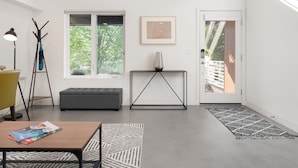 A modern living room with a grey sofa, a wooden coffee table, a floor lamp, and a large window with a view of trees.