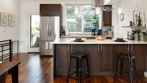 A modern kitchen with a large island, dark wood cabinets, stainless steel appliances, and a view of greenery outside.