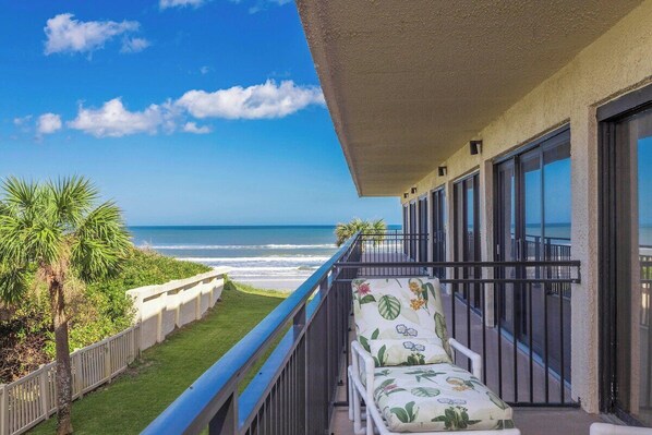 A balcony with a view of the ocean, a chair with a floral cushion, and a railing.