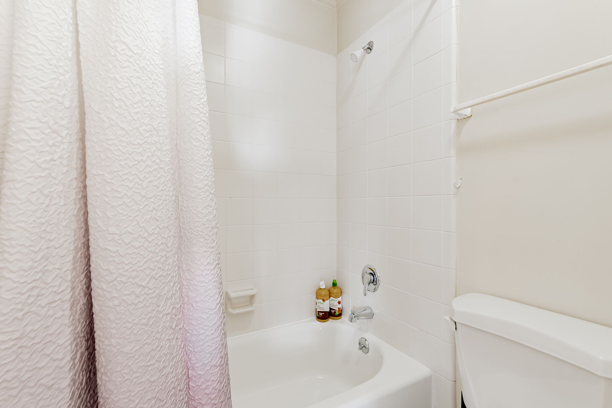 A bathroom with a white bathtub, a shower curtain, and two bottles of shampoo on the edge of the tub.