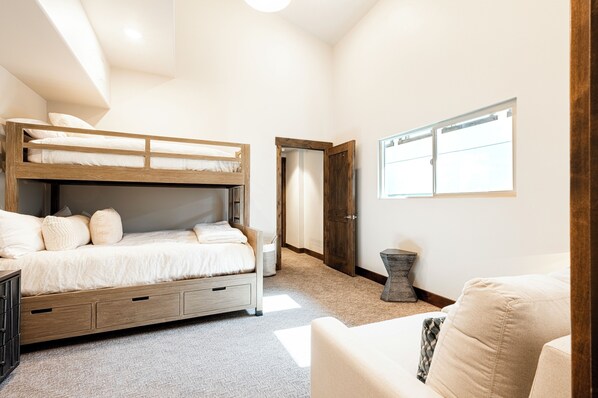 A bunk bed with storage drawers, a bedside table, a window with blinds, and a door leading to another room. - 3BR Top-Floor Condo with 3 Gas Fireplaces, Bunk Room & Heated Pool, Walk to Canyons Village (Park City)