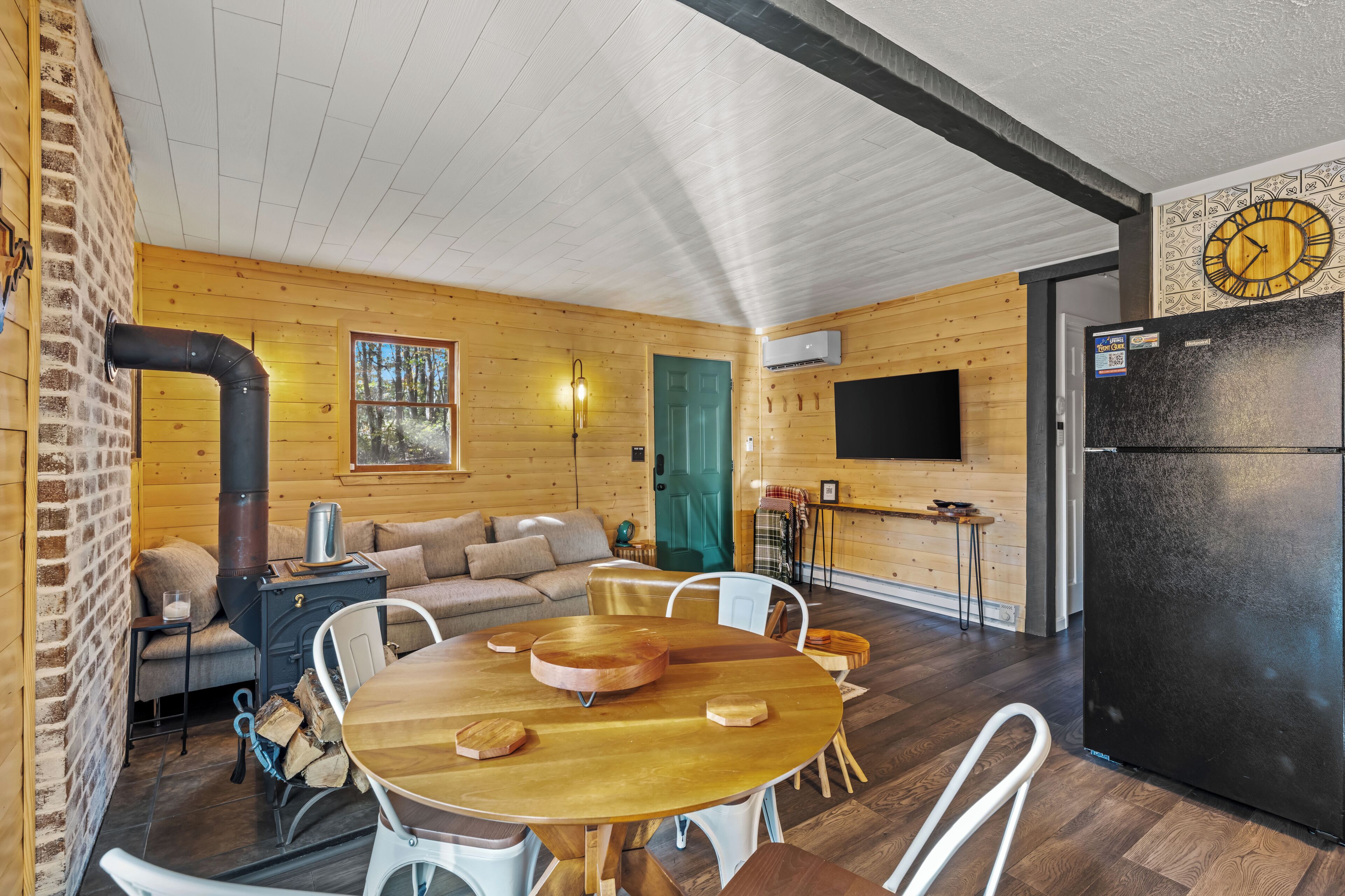 A cozy cabin interior with a dining table, sofa, and a large black refrigerator.