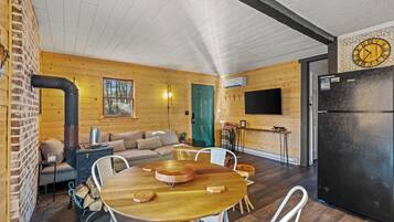 A cozy cabin interior with a dining table, sofa, and a large black refrigerator.