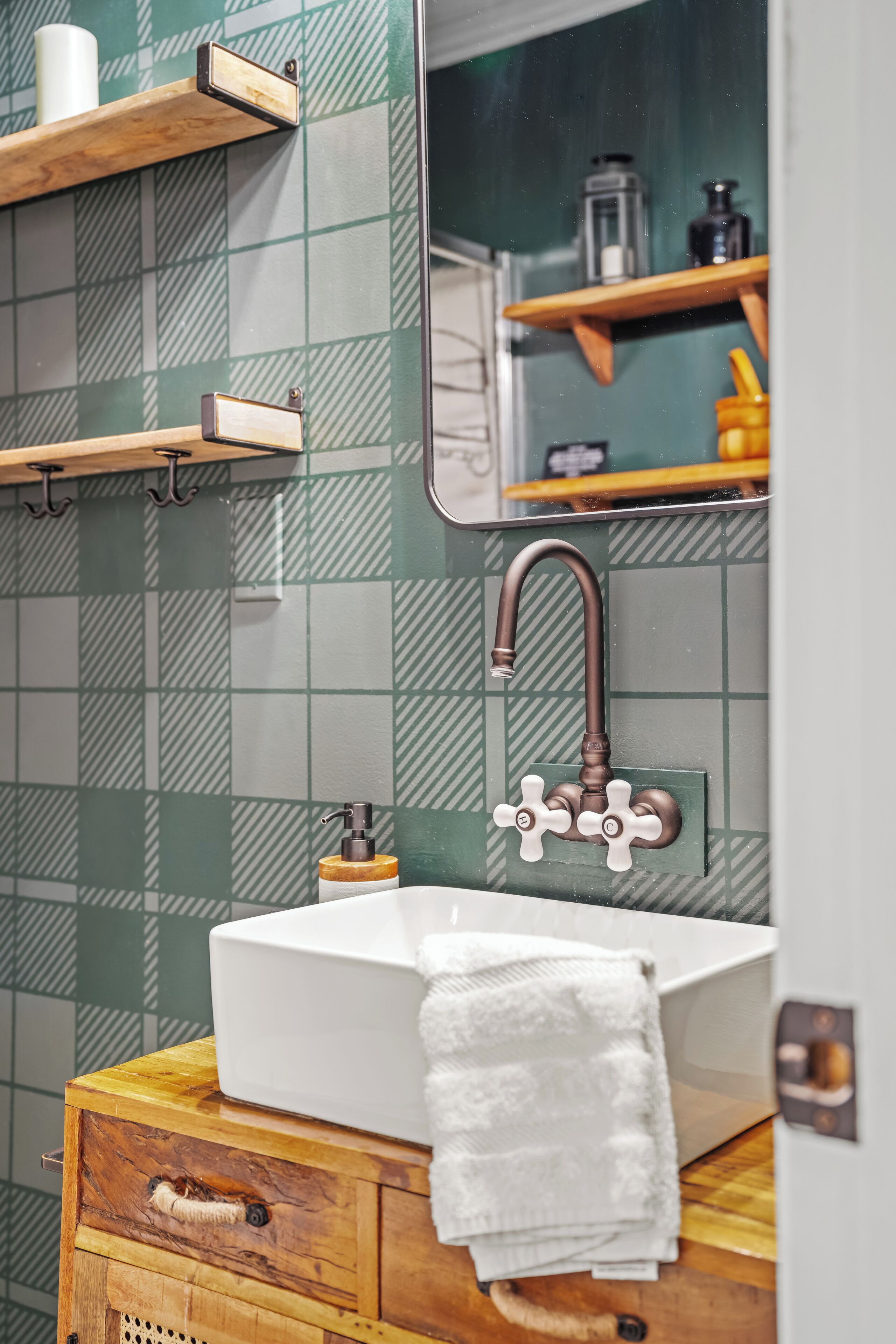 A bathroom with a white sink, a towel hanging on a wooden cabinet, and a mirror reflecting a shelf with toiletries.