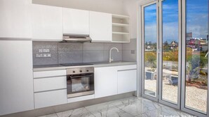 A modern kitchen with white cabinets, a stainless steel range, and a large window offering a view of the city. - Nissi Avenue Apartment in Ayia Napa (Ayia Napa)