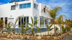A modern white building with solar panels, large windows, and tropical plants. - Nissi Avenue Apartment in Ayia Napa (Ayia Napa)