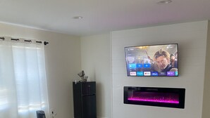 A modern living room with a flat-screen TV mounted on the wall, a black entertainment unit, and a large grey sectional sofa. - CG Suites (Columbus)