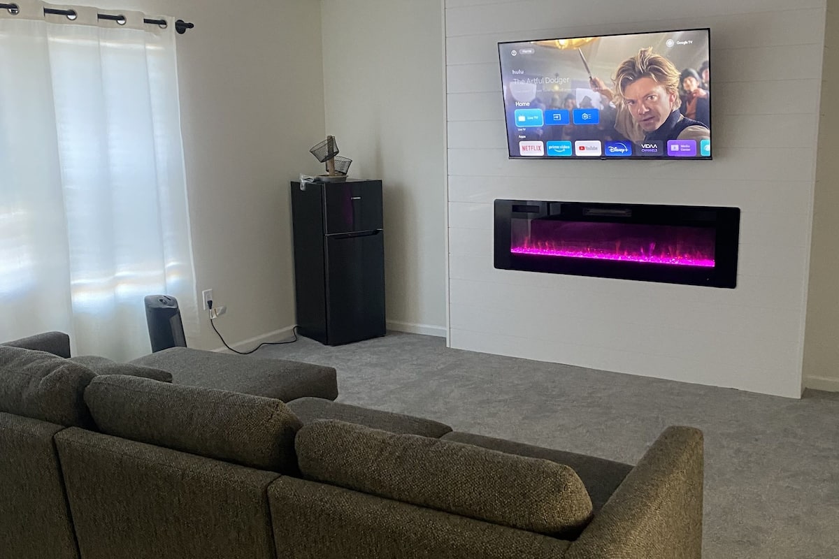 A modern living room with a flat-screen TV mounted on the wall, a black entertainment unit, and a large grey sectional sofa.