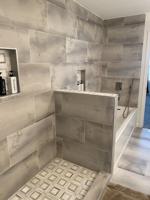 Une salle de bain moderne avec de grandes carreaux gris, un espace douche et un miroir agrémenté d’accessoires de toilette.