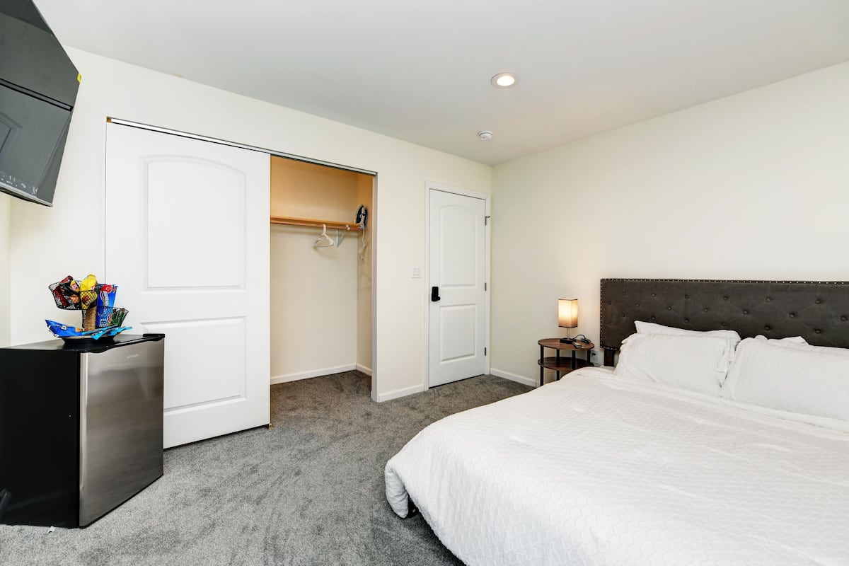 A hotel room with a large bed, a wardrobe, a desk with a lamp, and a TV mounted on the wall.