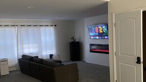 A modern hotel room with a large bed, a sofa, a TV, and a door. - CG Suites (Columbus)