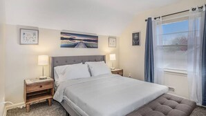 A bedroom with a large bed, two bedside tables with lamps, a window with curtains, and artwork on the walls. - The Park & River Chalet - Duplex 2 units (Detroit)