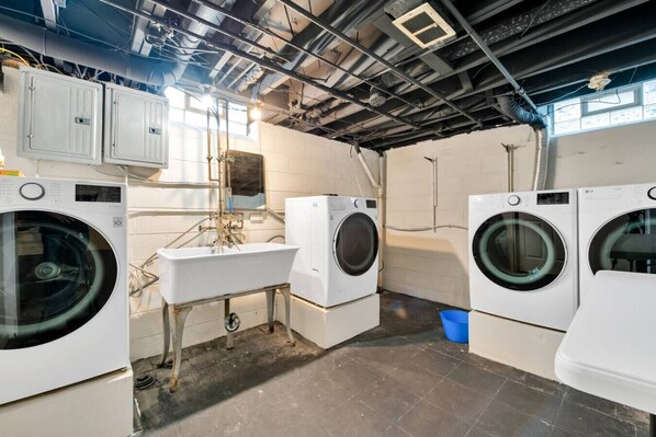 Een wasserette met meerdere wasmachines, een wasbak en zichtbare leidingen.