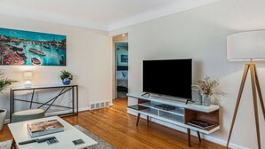 A modern living room with a flat-screen TV, a painting, and a bookshelf. - The Park & River Chalet - Duplex 2 units (Detroit)