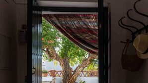 An open doorway leading to a courtyard with a large tree, a bench, and a hanging hat rack. - Rustic house with fireplace and wifi (Nigüelas)