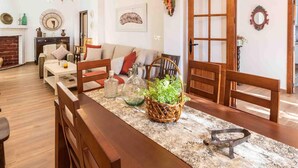 A cozy living room with a fireplace, a dining area with a wooden table and chairs, and a kitchen visible through an open door. - Rustic house with fireplace and wifi (Nigüelas)