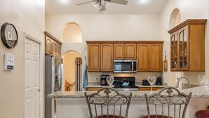 A kitchen with wooden cabinets, a microwave, and a refrigerator. There are two bar stools with red cushions.