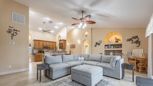 A spacious living room with a sectional sofa, a ceiling fan, and a kitchen in the background.