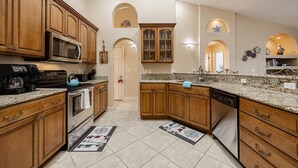 A kitchen with wooden cabinets, granite countertops, a microwave, stove, and dishwasher. There are two doorways leading to other rooms.