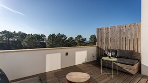 A rooftop terrace with a wooden deck, a sofa, a small round table with wine glasses, and a wooden fence. - Rooftop Terrace Apartment - Beach House Clerigo by Lisbeyond (Aljezur)