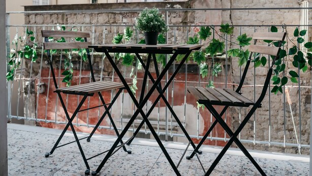 A balcony with a metal table and two wooden chairs, a potted plant, and a view of surrounding buildings. - Brombeis by Casa Napoletana, with patio H. center (Napoli)