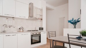 A modern kitchen with white cabinets, stainless steel appliances, and a dining area with a table and chairs. - Brombeis by Casa Napoletana, with patio H. center (Napoli)