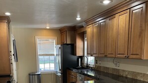 A kitchen with wooden cabinets, a black countertop, and a stainless steel refrigerator. - Come stay at Suzie's House!<br>Spacious Family-Friendly 4-Bedroom Home (Fort Benton)