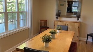 A dining room with a wooden table, chairs, potted plants, a bench, and a large window. - Come stay at Suzie's House!<br>Spacious Family-Friendly 4-Bedroom Home (Fort Benton)