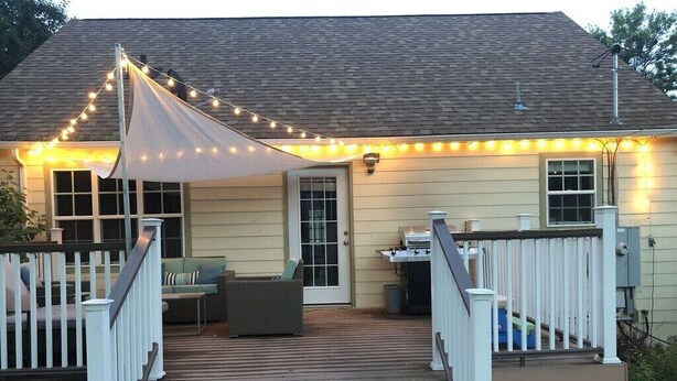 A house with a wooden deck, white railing, and string lights. - Come stay at Suzie's House!<br>Spacious Family-Friendly 4-Bedroom Home (Fort Benton)