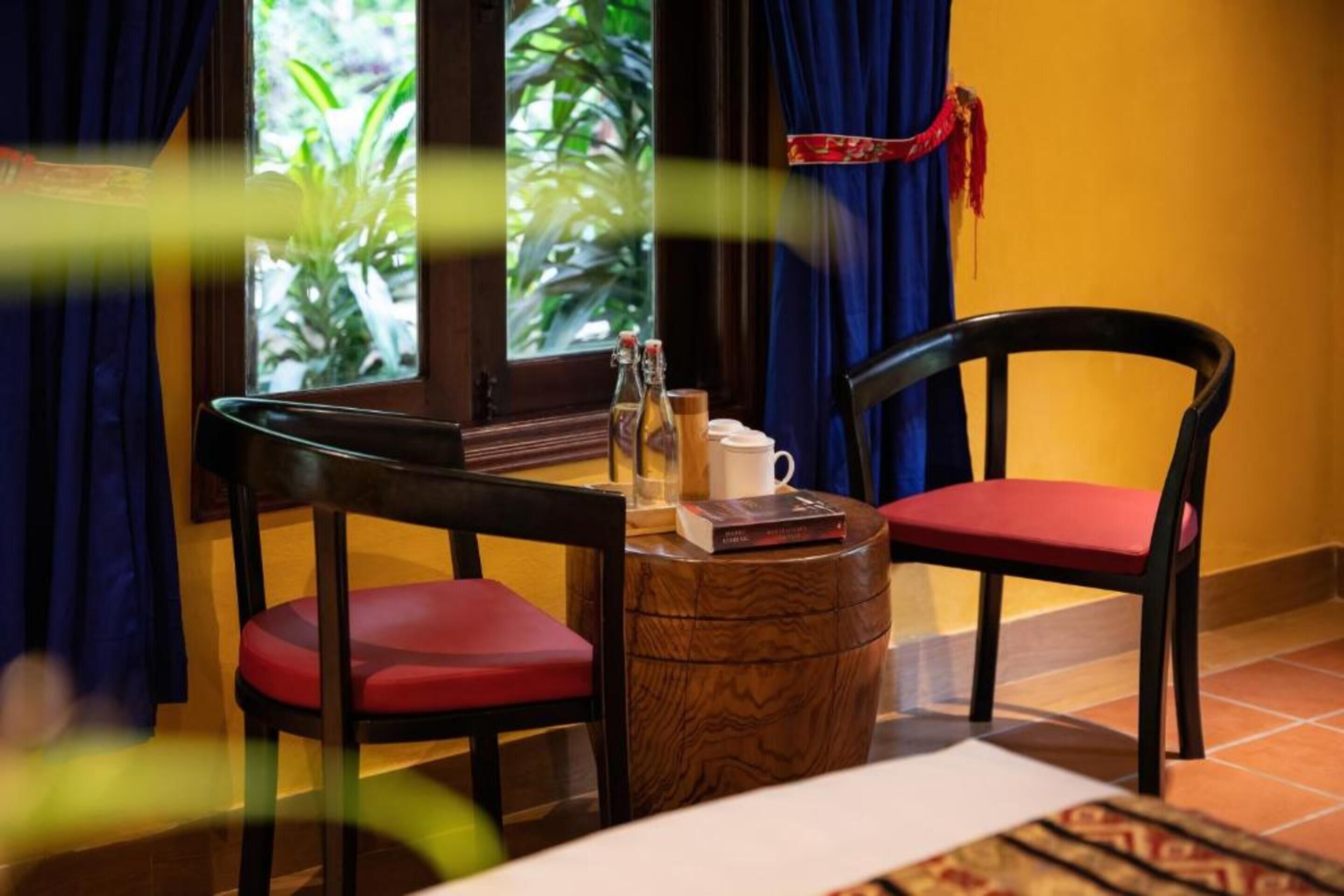Une pièce avec deux fauteuils rouges rembourrés, une petite table en bois et une fenêtre avec des rideaux.