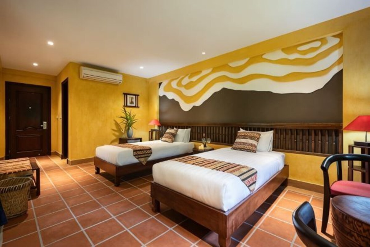 Habitación de hotel con dos camas, una silla, una mesa y un adorno en la pared.