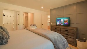 Ein Schlafzimmer mit Bett, Fernseher, Kleiderschrank und angrenzendem Badezimmer.
