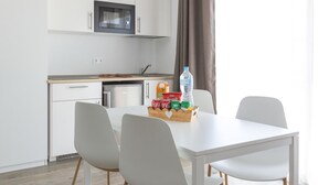 Moderni keittiö, jossa on valkoiset kaapit, mikroaaltouuni, astianpesukone sekä ruokailutila, jossa on valkoinen pöytä ja tuolit.