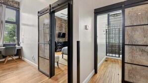 A modern interior with a sliding door leading to a bedroom, a desk with a chair, and a TV in the background. - A Cleveland Modern and Historic Apartment (Cleveland)