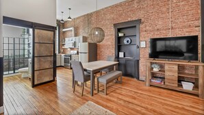 A modern kitchen with a brick wall, wooden flooring, and a dining area with a table and chairs. - A Cleveland Modern and Historic Apartment (Cleveland)