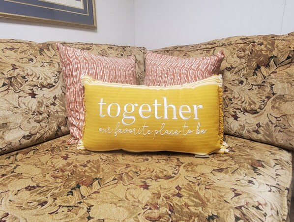 Un sofá con estampado floral y dos almohadones decorativos, uno con la inscripción "together our favorite place to be".