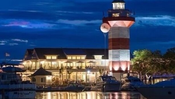 A waterfront hotel with a prominent lighthouse tower, reflecting in the calm water. - Spacious Condo in the heart of Harbor Town! (Hilton Head Island, USA)