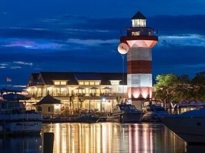 Un hotel frente al agua con una llamativa torre de faro, reflejada en aguas tranquilas.