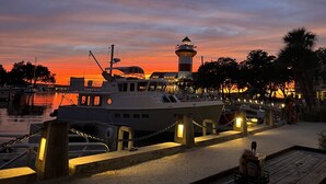 A marina at sunset with a lighthouse, boats, and a docked yacht. - Spacious Condo in the heart of Harbor Town! (Hilton Head Island, USA)