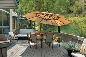 Eine Holzterrasse mit Tisch, Stühlen, einem Whirlpool und einem großen Sonnenschirm.