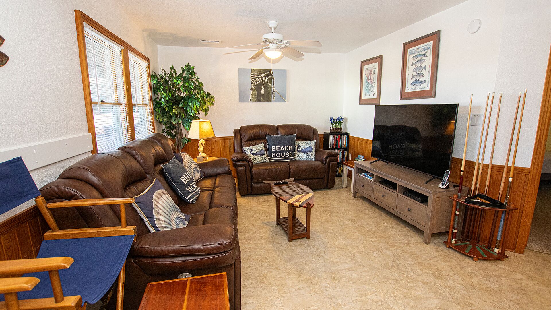 A living room with a brown leather sofa, a wooden coffee table, a TV stand, and a ceiling fan.