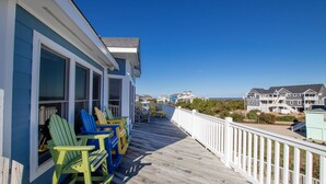 A wooden deck with colorful Adirondack chairs, a white railing, and a view of beach houses in the background. - Oceanside, 7 BRS, Private Pool, Hot Tub, Rec Room, OS1A, Corolla Horizons (Corolla)